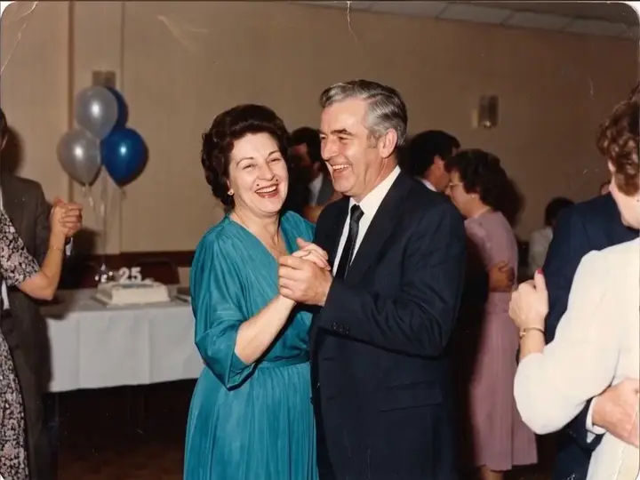 A couple in their fifties dancing at a party, balloons behind them.